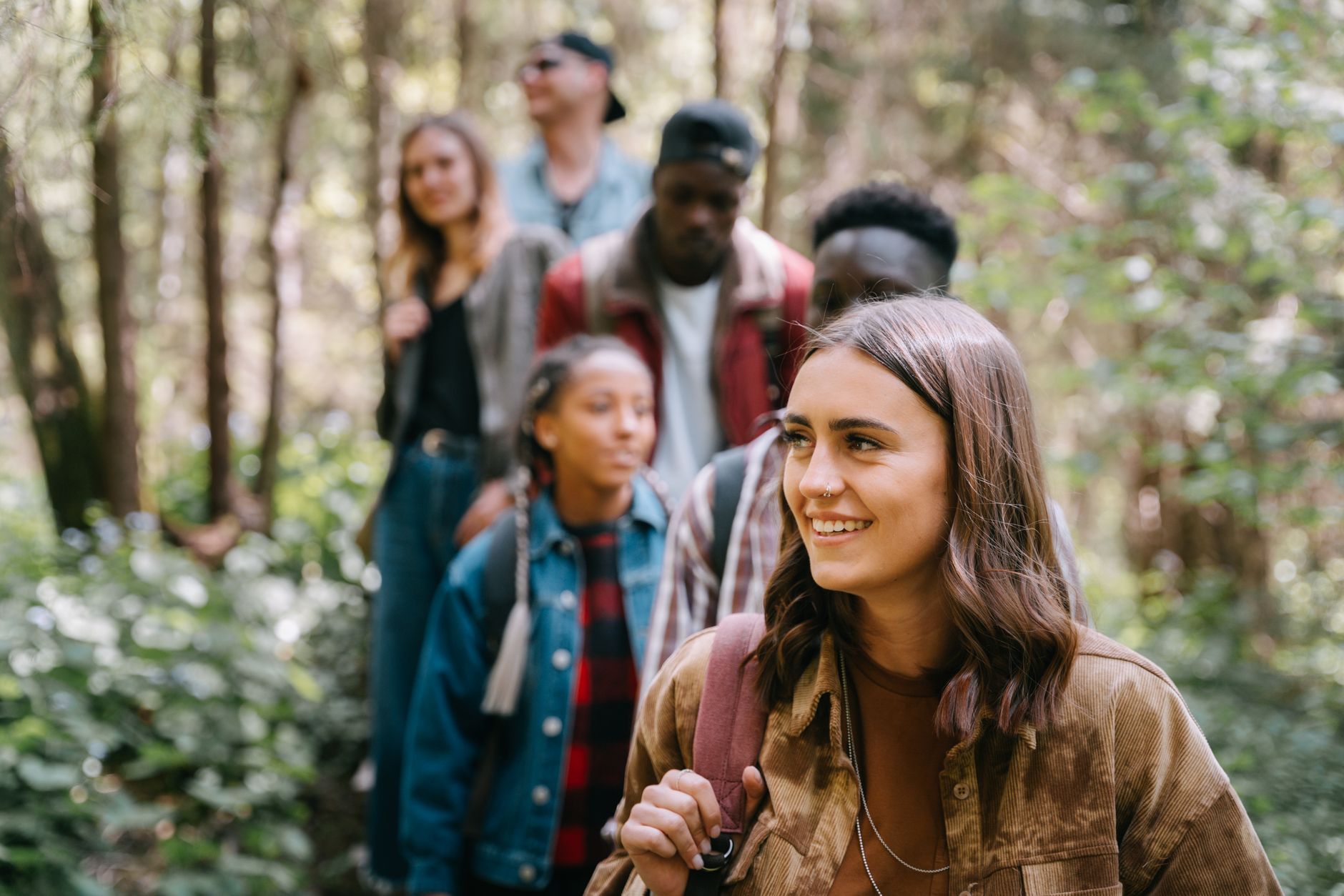 Five friends enjoying a hike through a lush, green forest on a sunny day.
