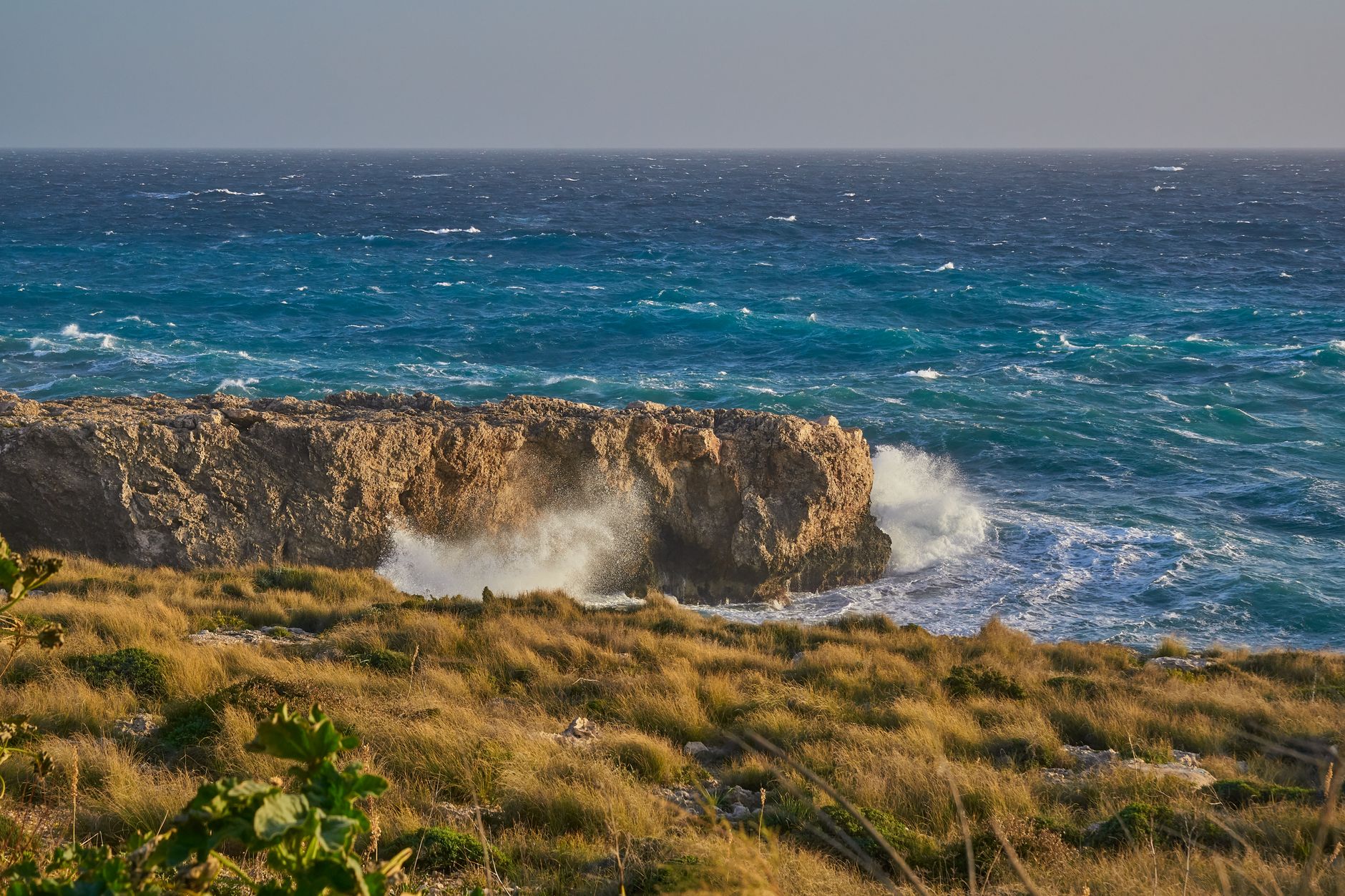 Dramatic view of Malta's coastline, featuring rugged limestone cliffs and crashing waves under a bright sky.