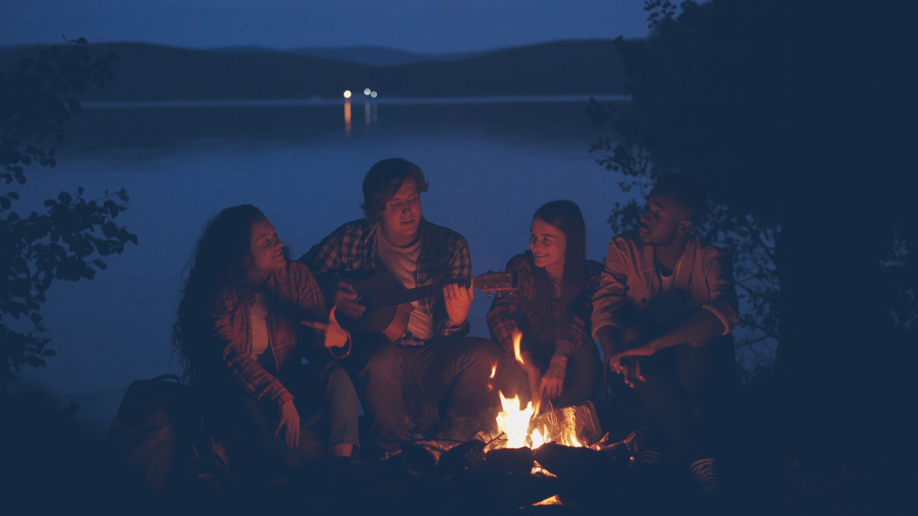 A group of friends sharing a campfire by the lake, playing guitar under a starlit sky.