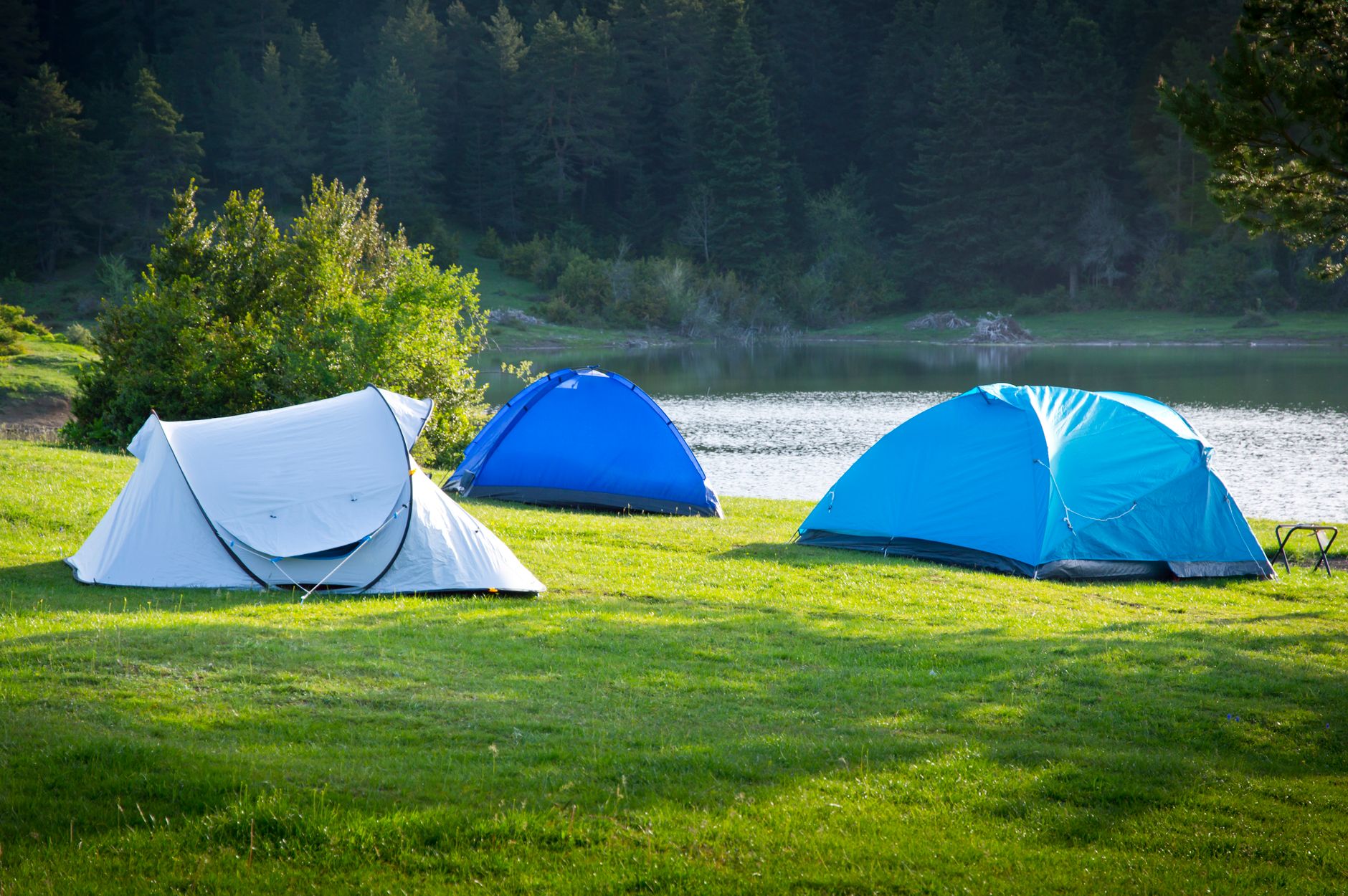 Serene campsite with tents by a forested lake, perfect for a summer outdoor adventure.