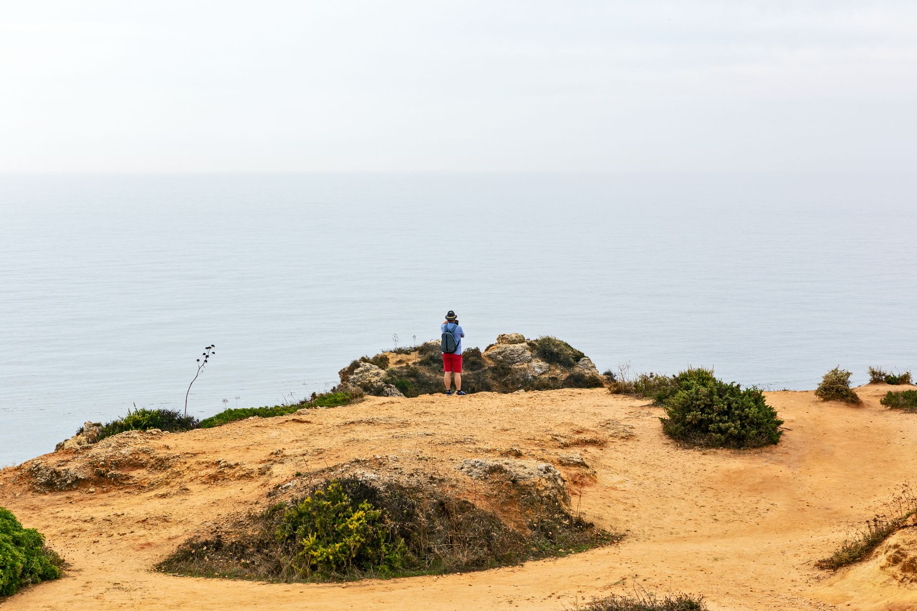 Person in blue jacket on cliff in Lagos, Portugal, gazing at the vast ocean.