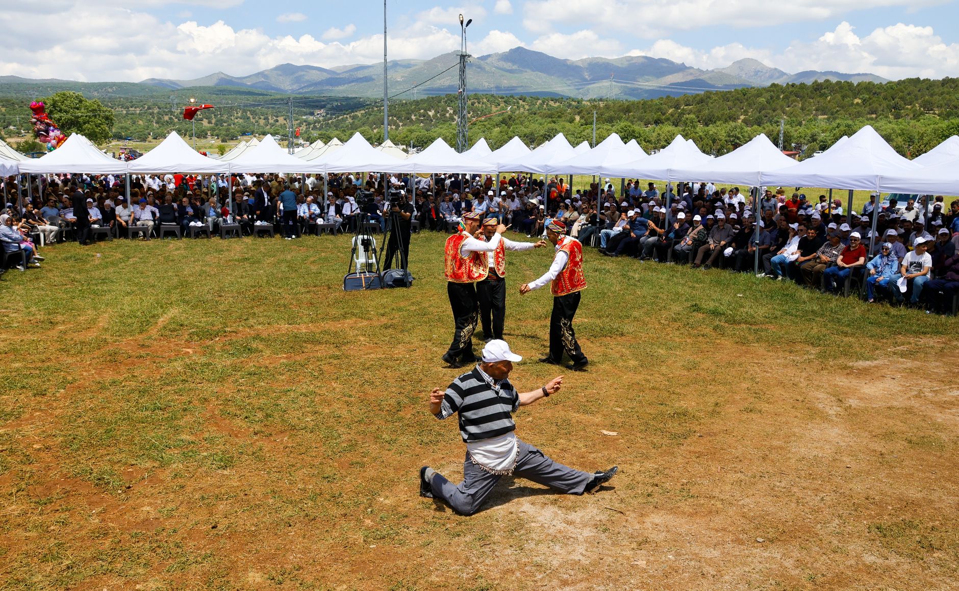 Capturing a lively cultural dance performance at an outdoor festival under tents with a scenic mountain backdrop.