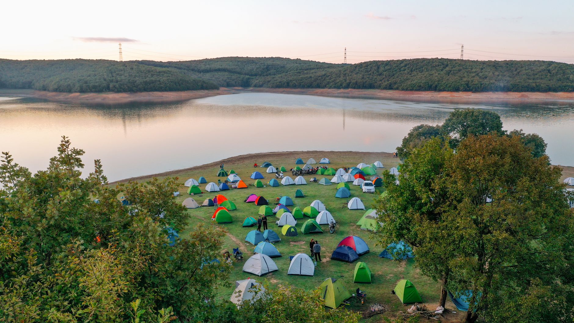 Vibrant tents set up by a tranquil lake amidst lush greenery during sunset, perfect for outdoor adventures.
