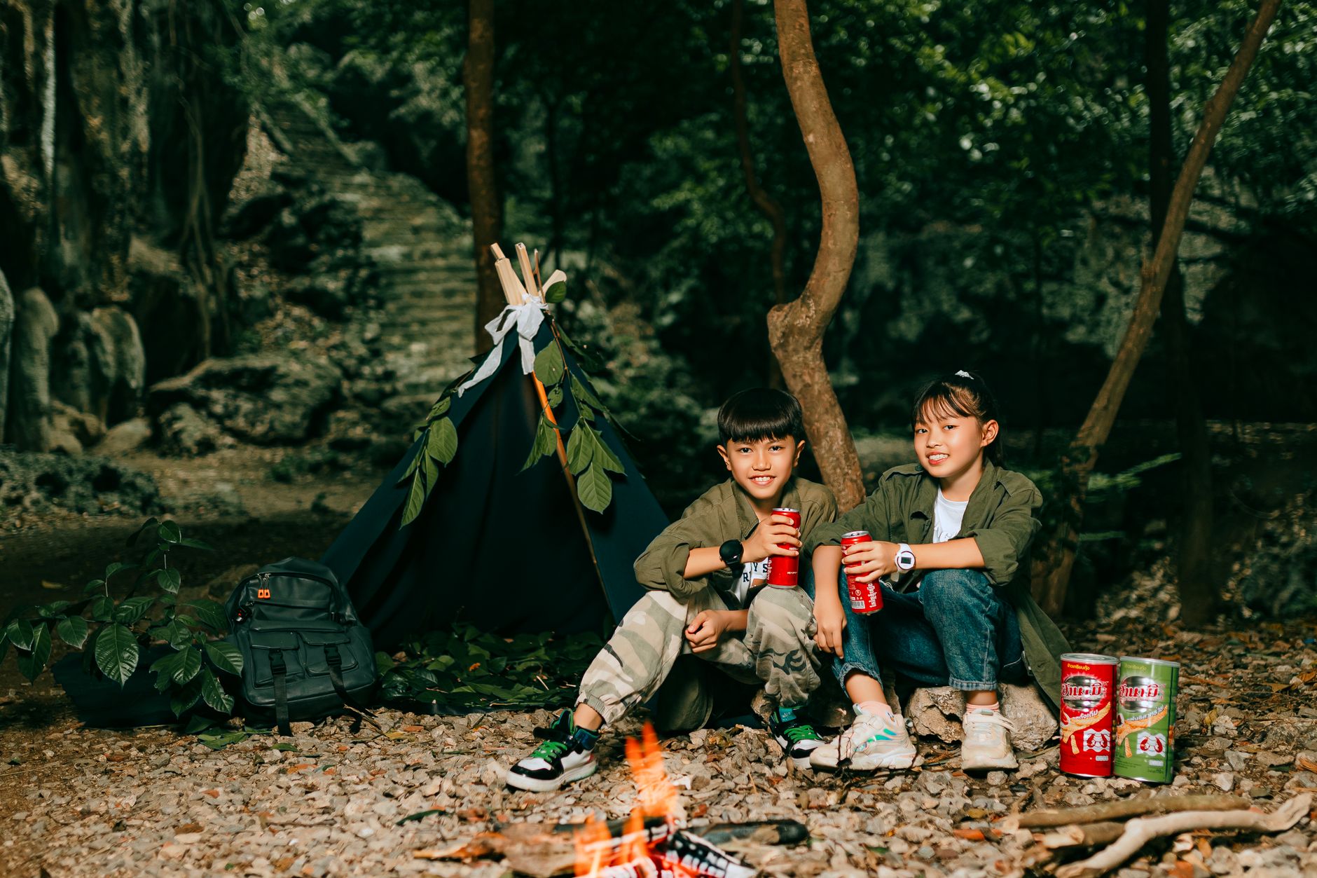 Kids relaxing by a bonfire in a forest campsite, enjoying snacks and nature.
