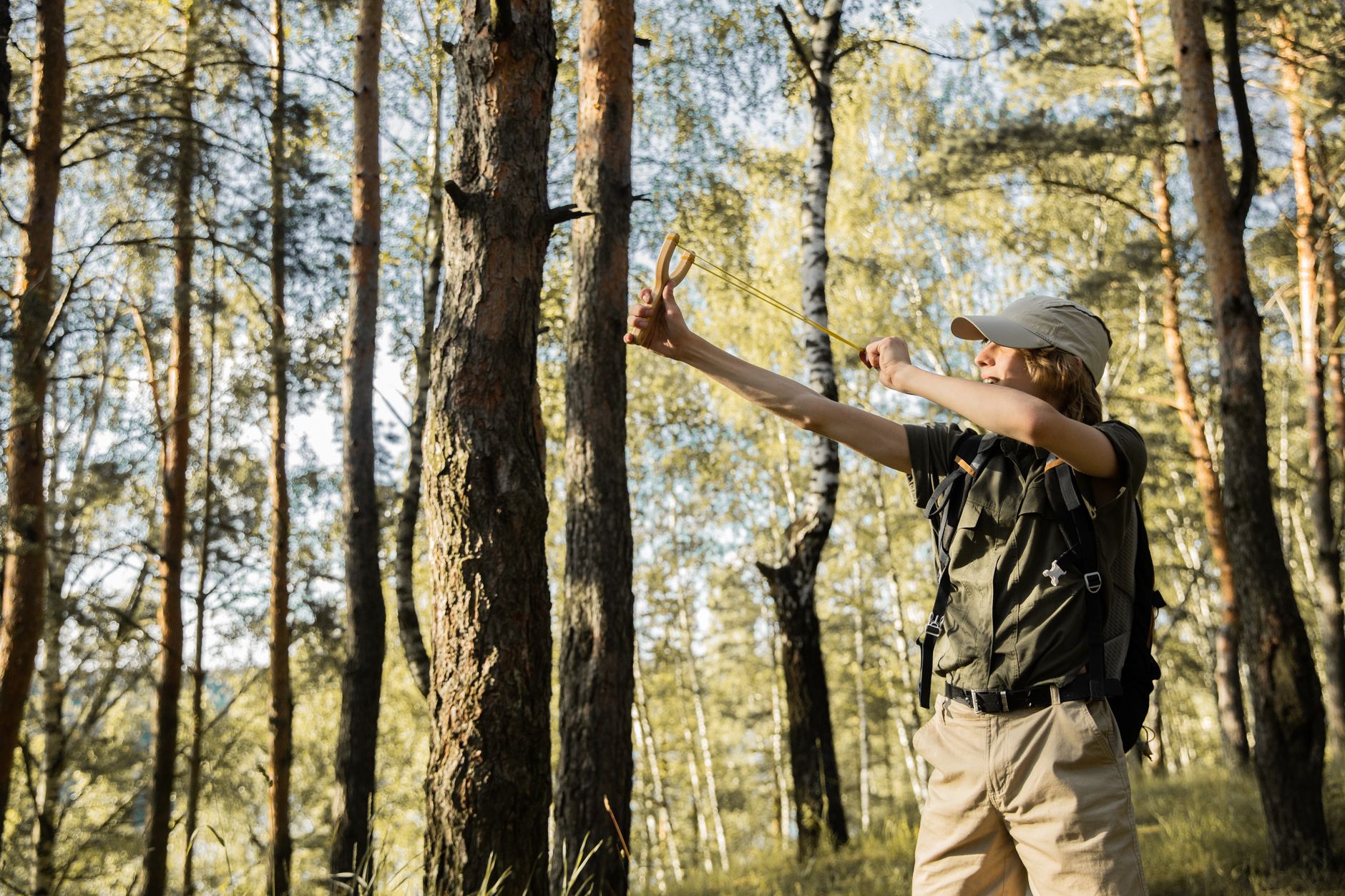 A teenager skillfully uses a slingshot in a sunlit forest during a summer outing.