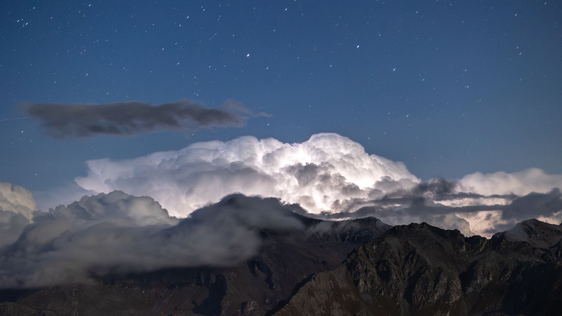 Stunning nighttime mountain scene with clouds and stars creating a magical landscape.