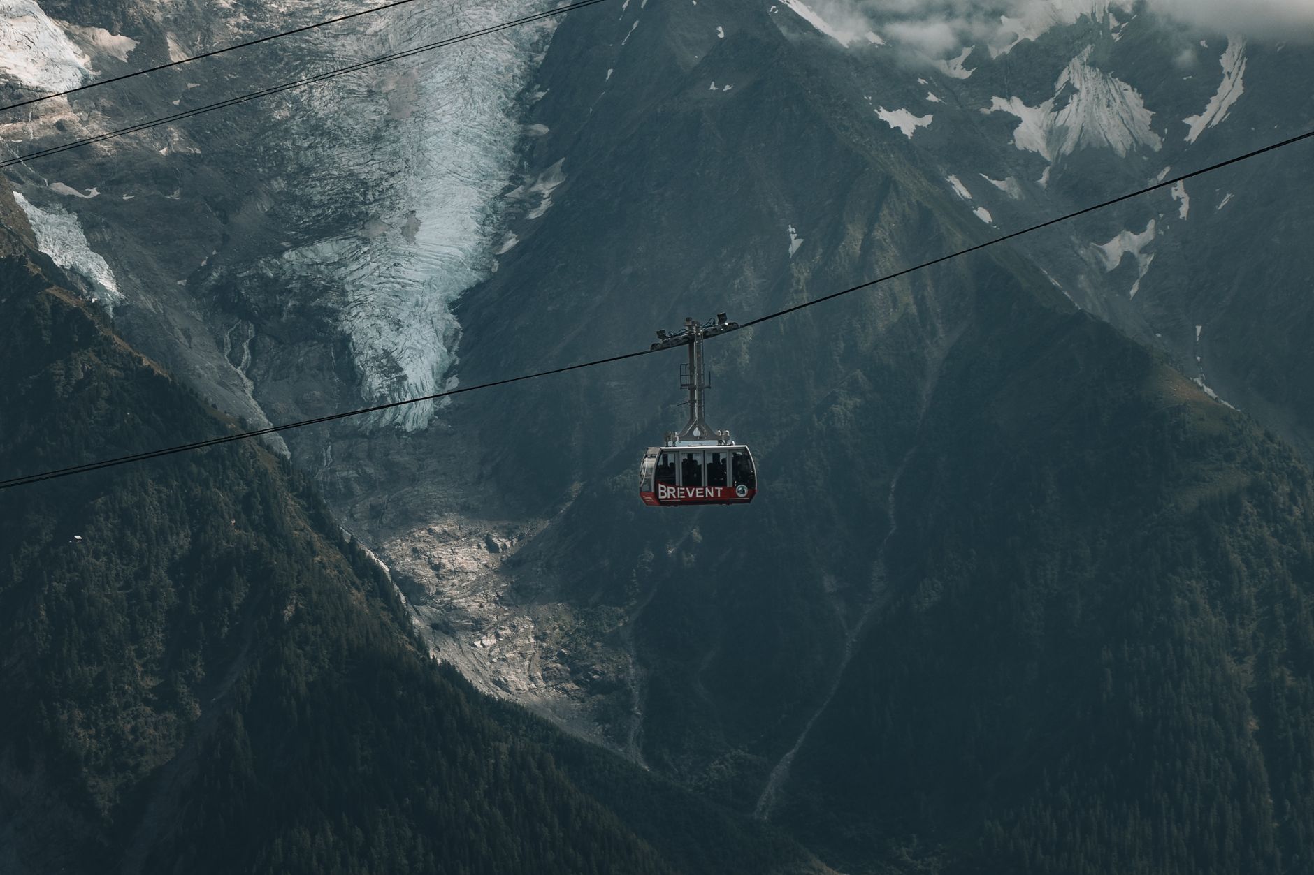 A breathtaking view of a cable car in the alpine mountains with snowcapped peaks and a glacier.