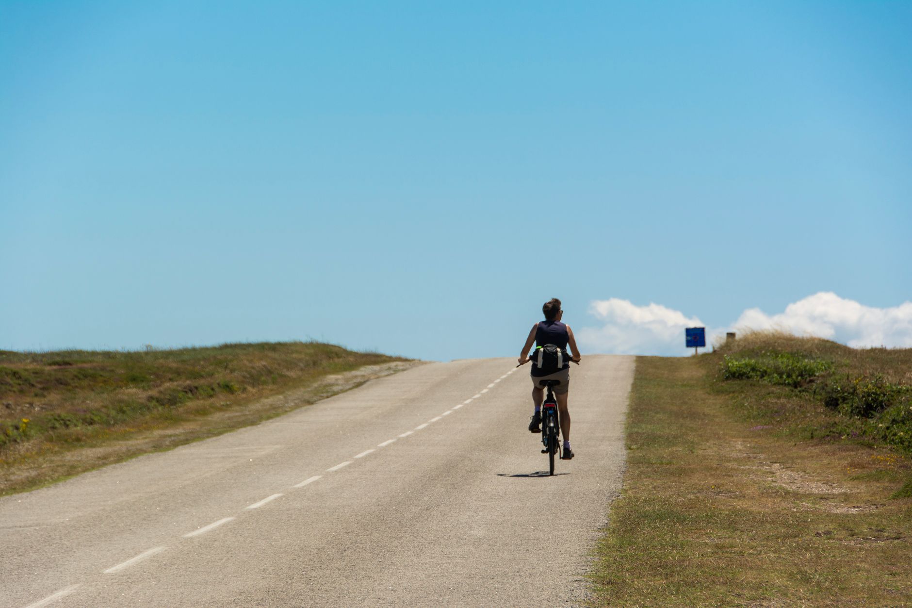 A lone cyclist rides uphill on a sunny day, capturing the essence of a solo adventure.