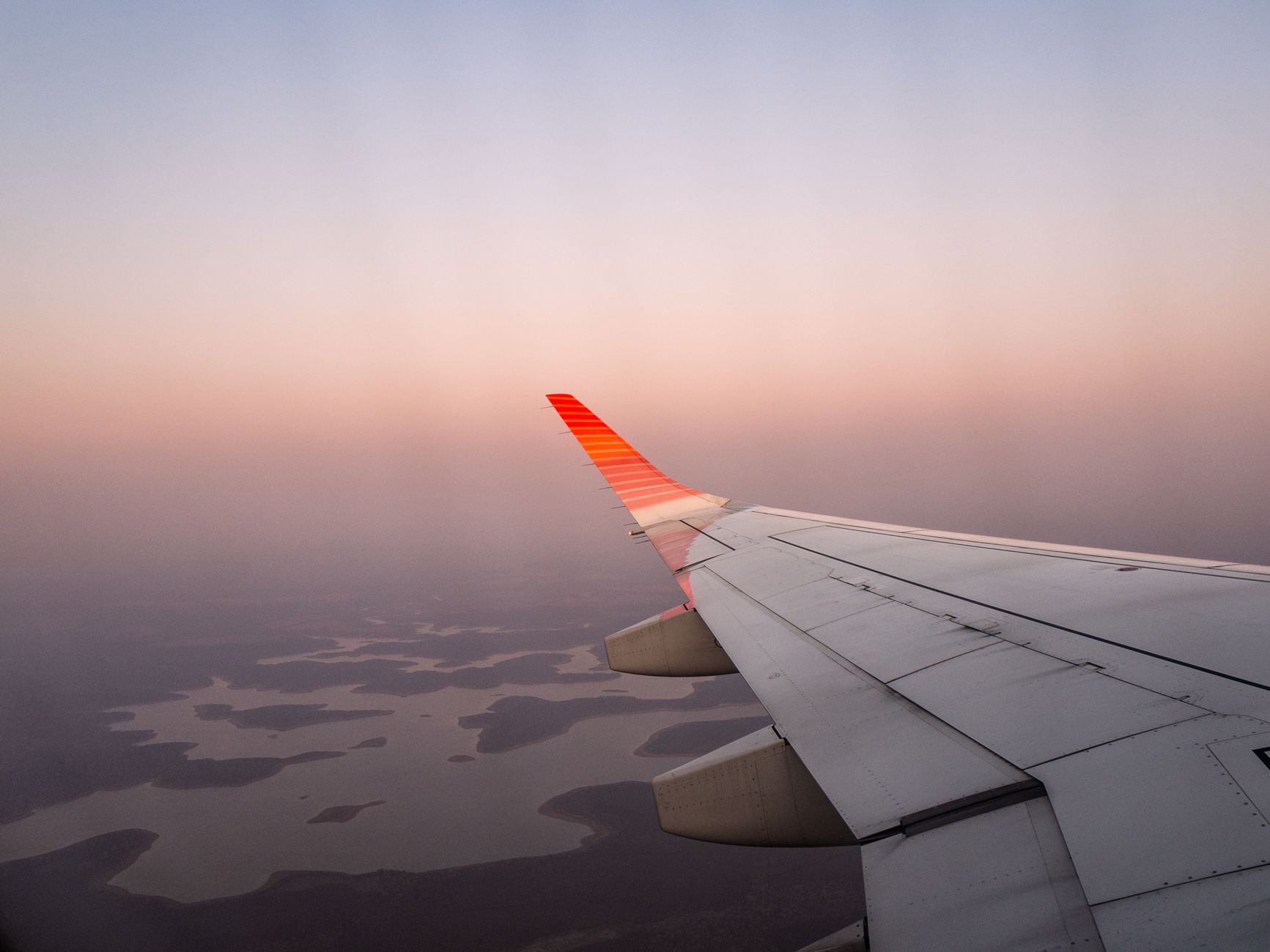 A scenic aerial view of an airplane wing flying over a landscape during sunset.