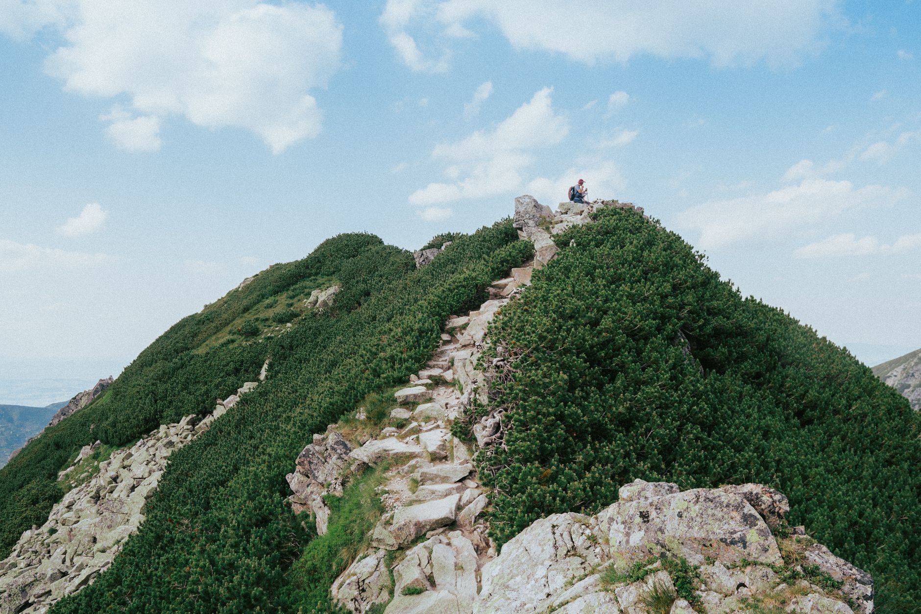 Rocky trail leading to a mountain peak in the Tatra Mountains, with clear skies and lush greenery.
