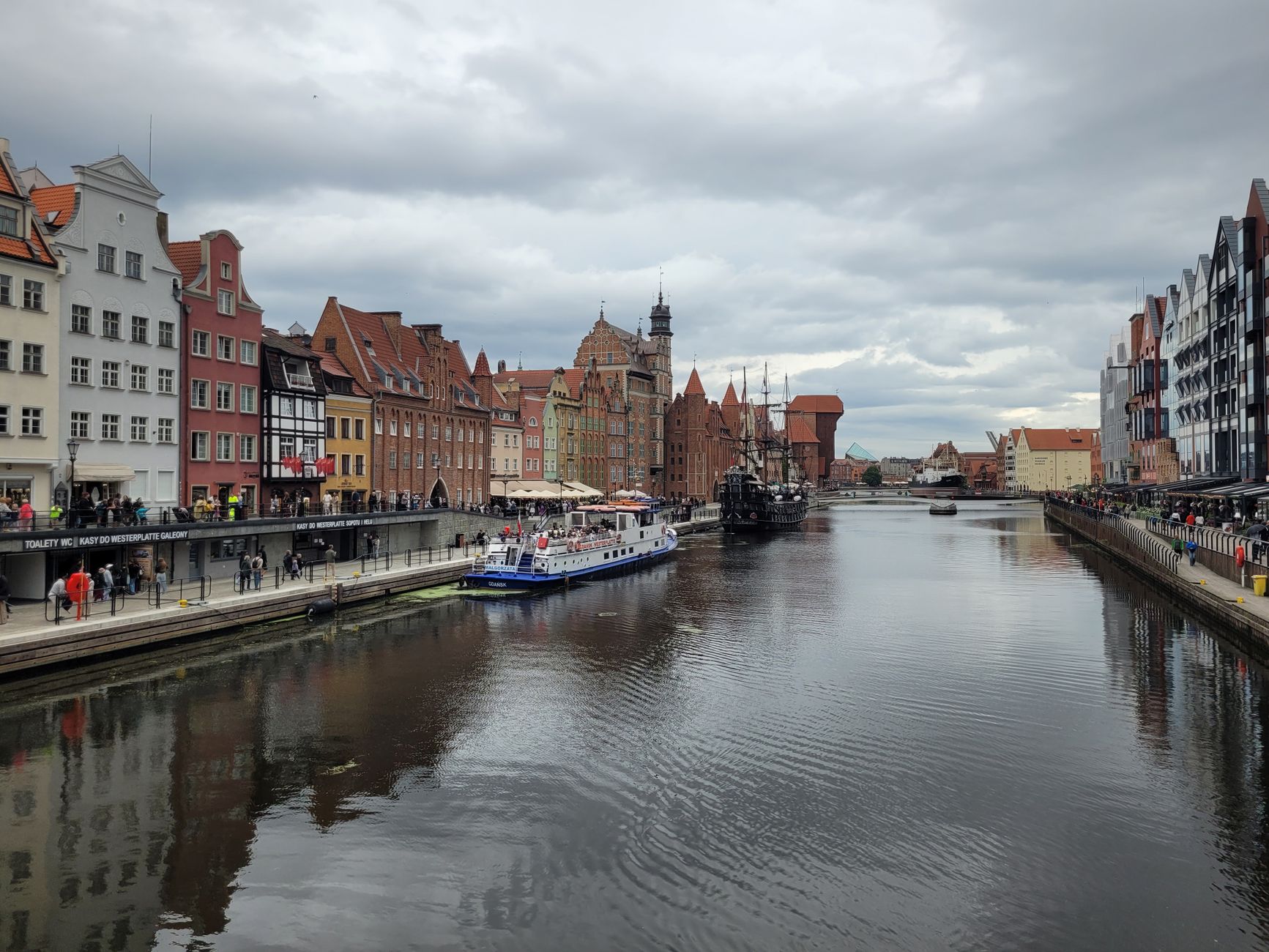 Charming view of Gdańsk's waterfront with historic architecture along the river on a cloudy day.