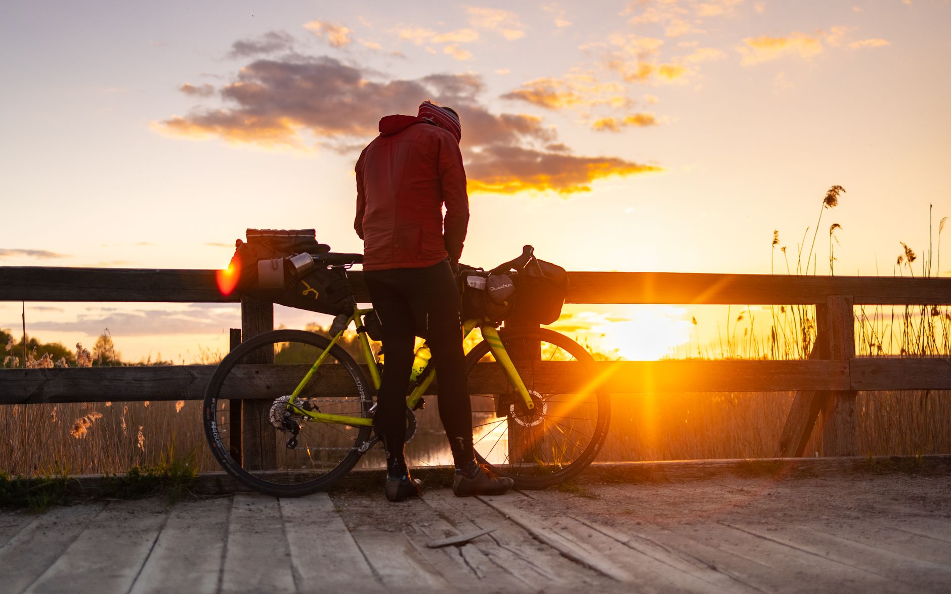 A cyclist with a packed bike enjoys a tranquil sunset by a lake, highlighting adventure travel.