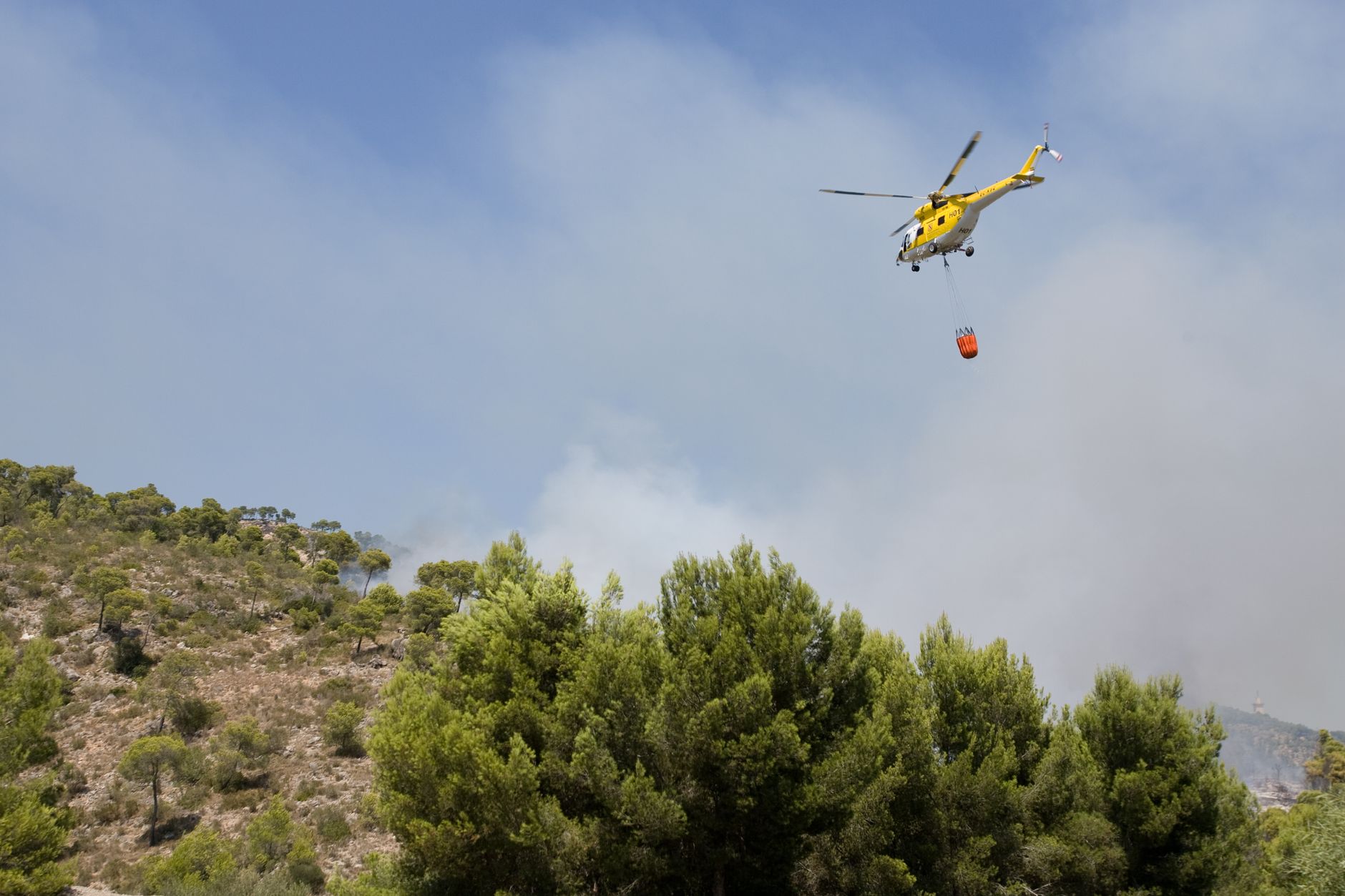 A helicopter combats a forest wildfire in Spain, releasing water over the blazing area.