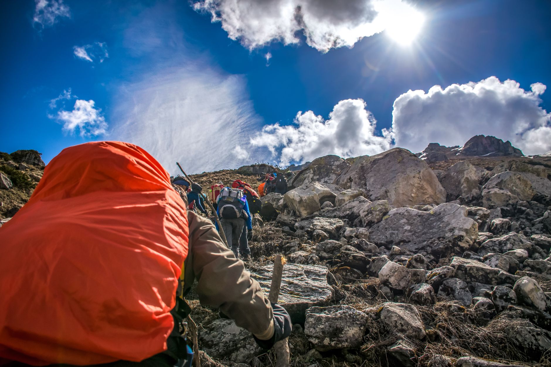 Hikers ascending a rocky mountain trail under a bright sunlit sky.