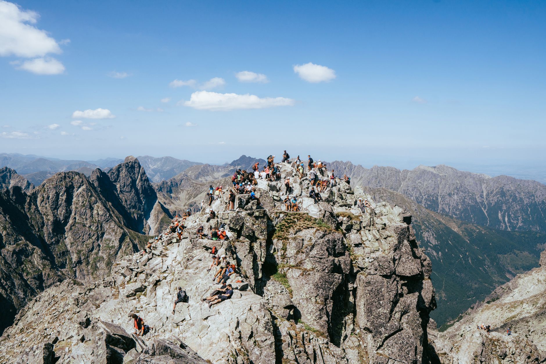 A group of hikers on a rocky peak in the Tatra Mountains under a bright blue sky.