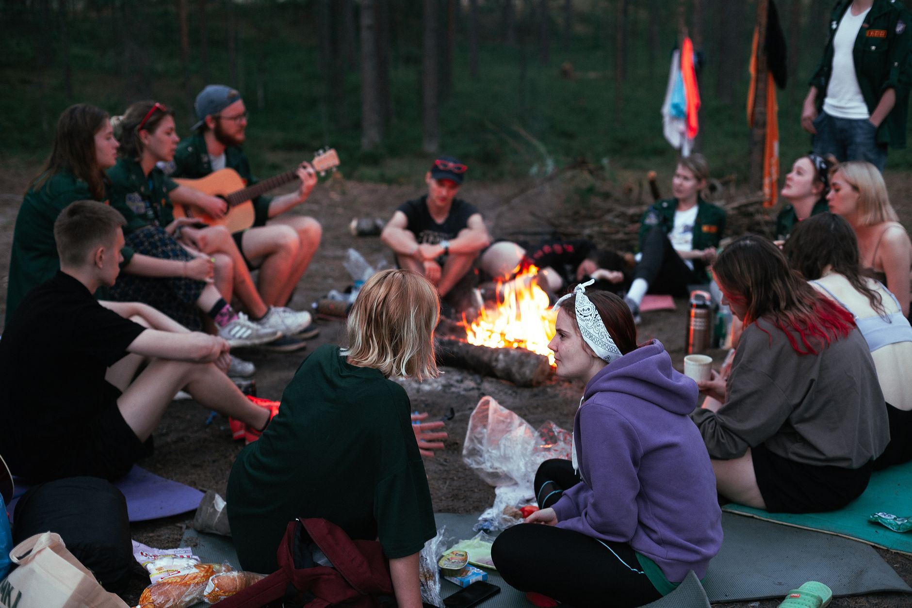 A diverse group of friends enjoying a campfire gathering in the forest during the evening.