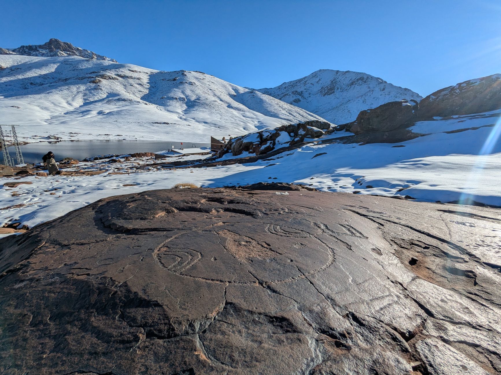 A breathtaking view of ancient rock art on a mountainside covered with snow under a clear blue sky.