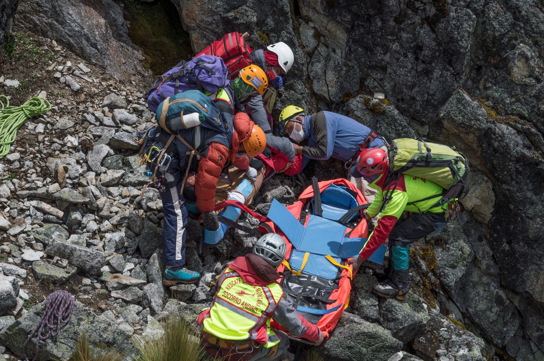 Rescue team assisting injured hiker on rocky mountainside with stretcher.