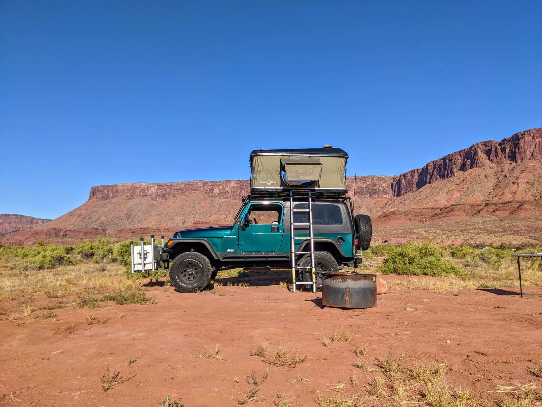 A Jeep with a rooftop tent setup in the scenic Castle Valley, Utah, under a clear blue sky.