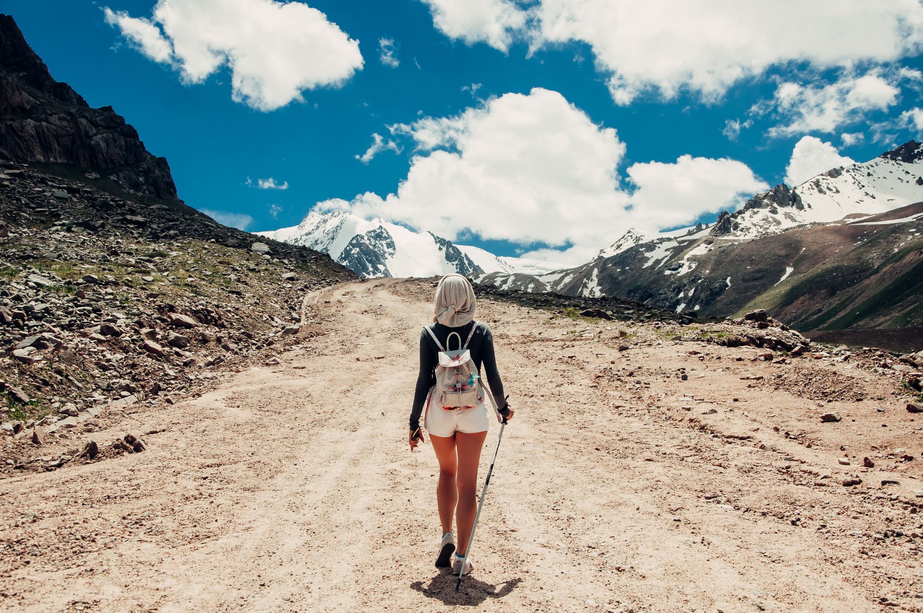 Back view of a woman hiking on a scenic mountain trail during daylight.
