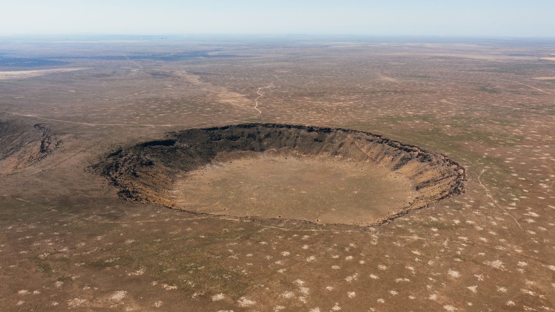 Aerial photograph of a vast, barren meteor crater in an arid landscape, showcasing nature's raw terrain.