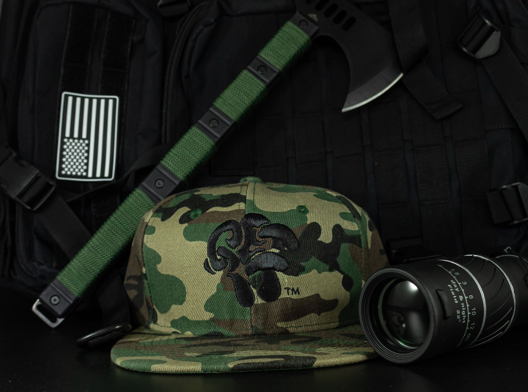 Close-up photo of camouflage cap placed with tactical gear and camera lens.