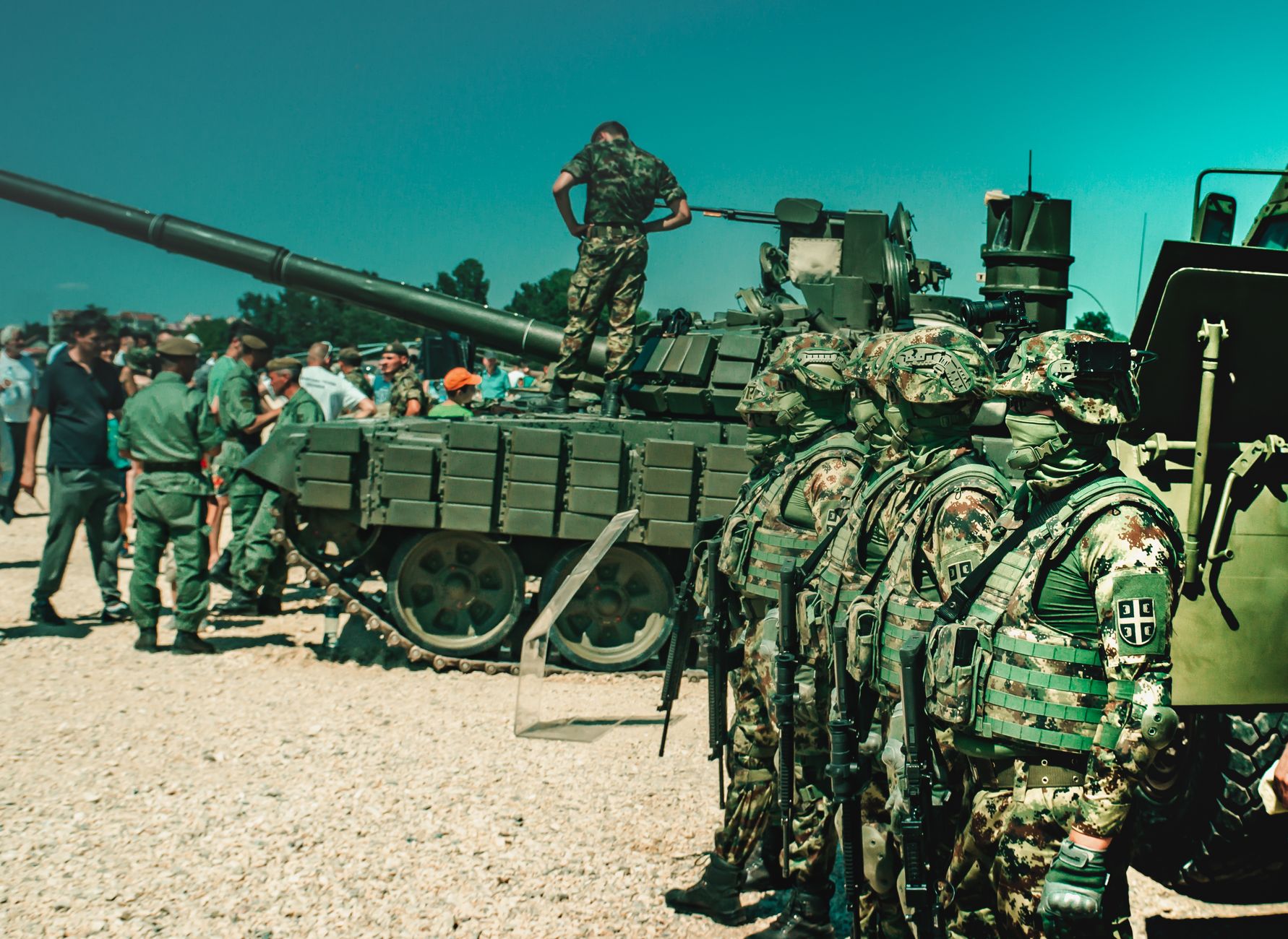 Group of camouflaged soldiers near a tank during a training exercise outdoors.