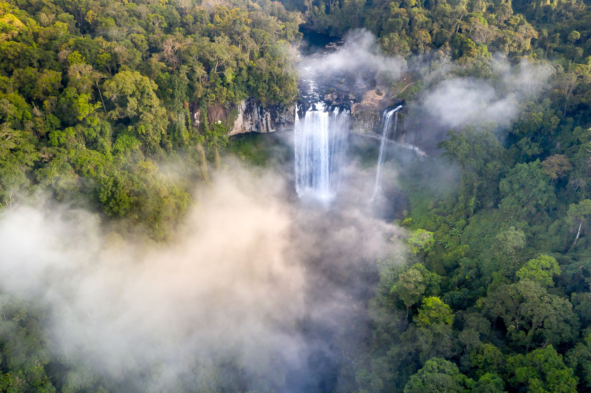 A breathtaking aerial view of a waterfall surrounded by mist and lush rainforest.