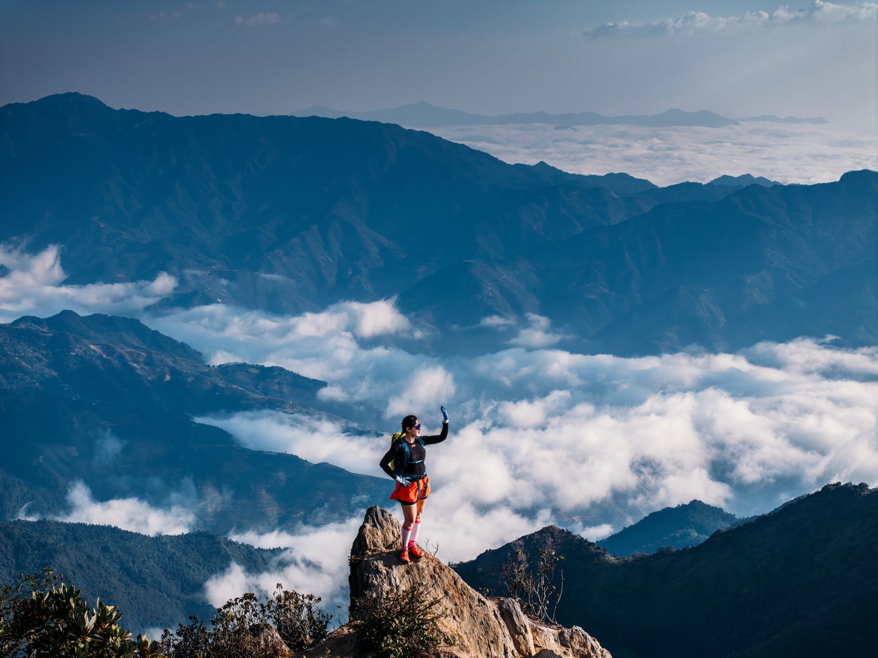 A hiker triumphantly standing on a mountain peak above the clouds, capturing the breathtaking view.