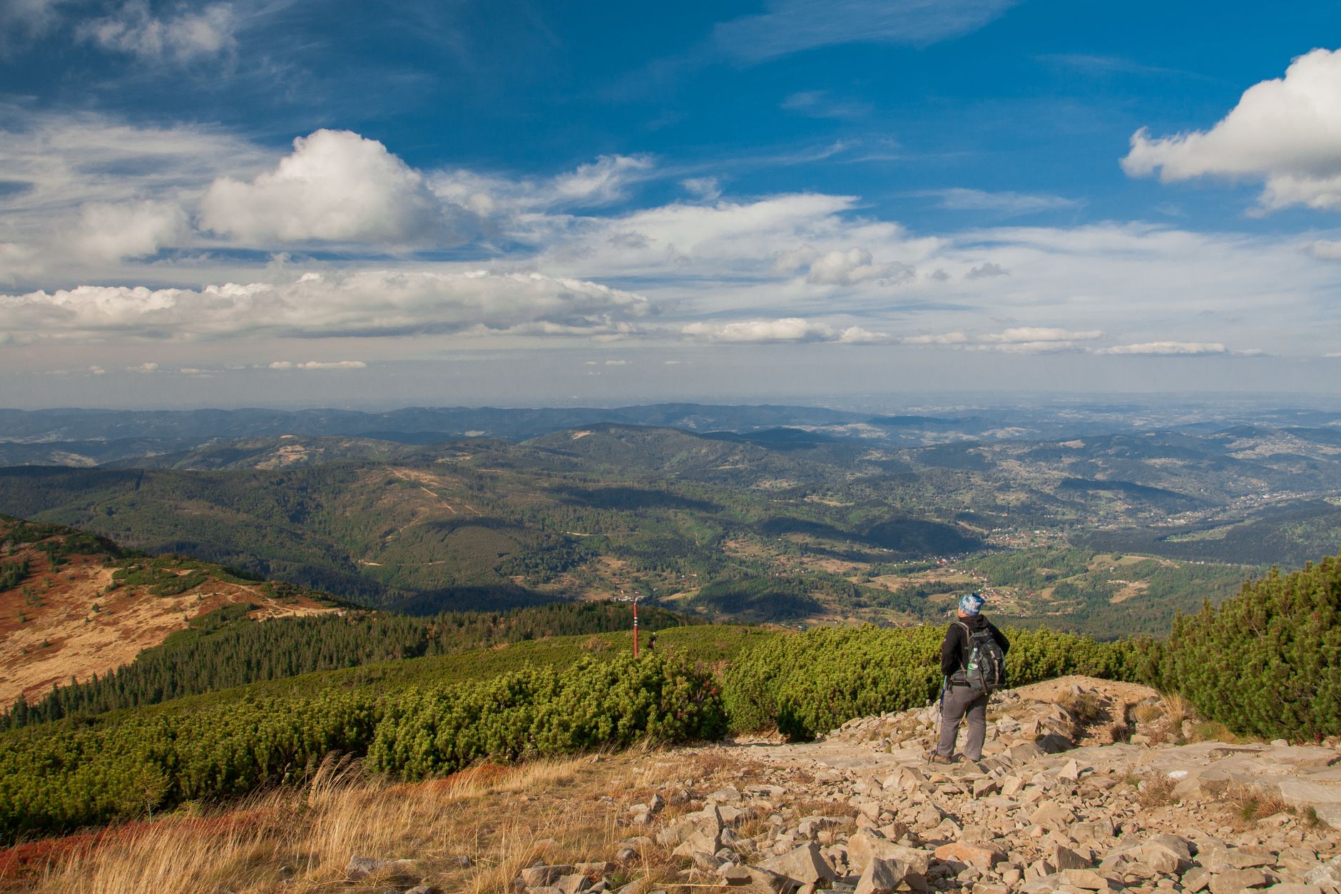 A hiker enjoys a panoramic view of the Beskid Mountains in Poland under a bright blue sky.