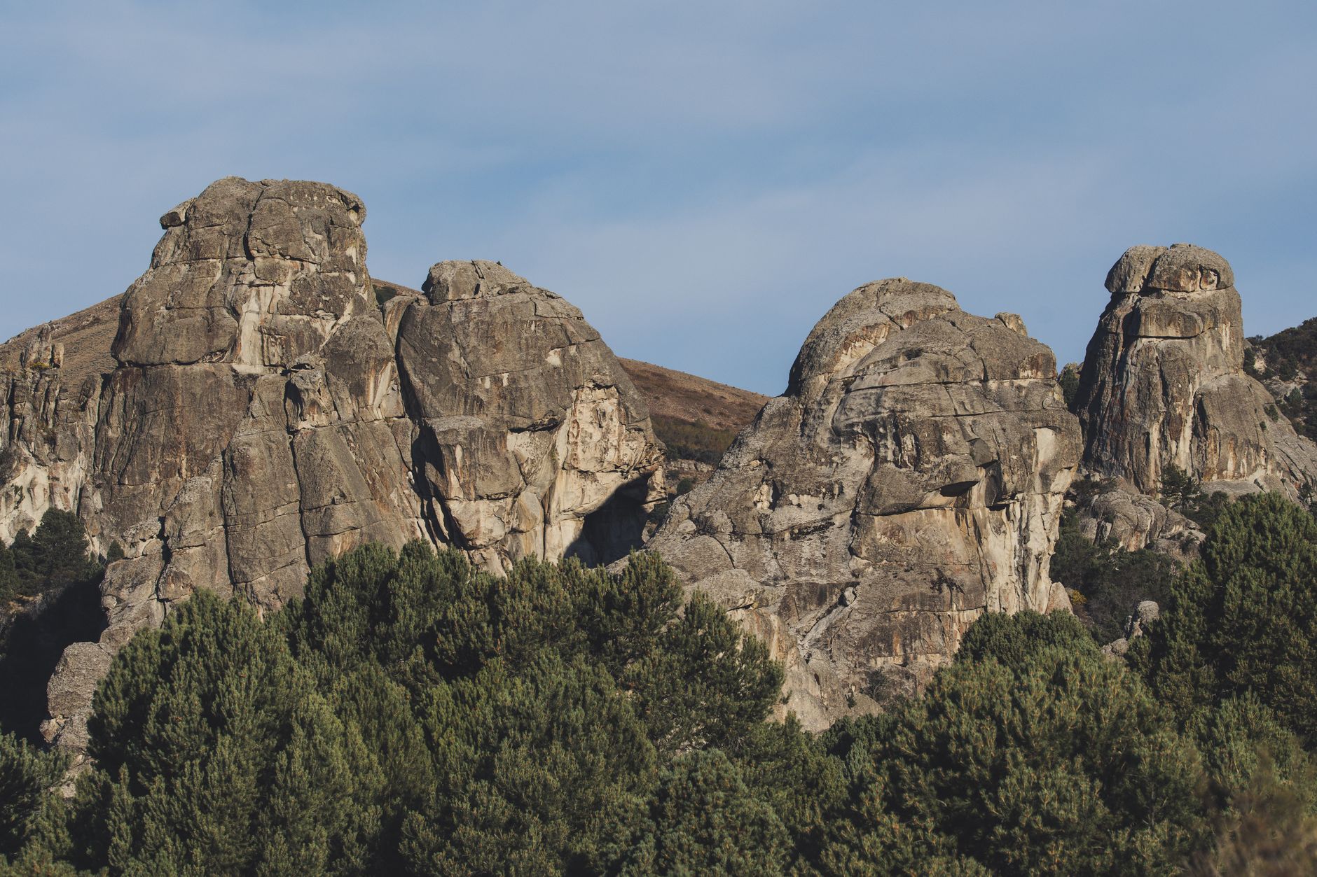 Majestic rocky formations rise above lush pine trees in a serene mountainous setting.