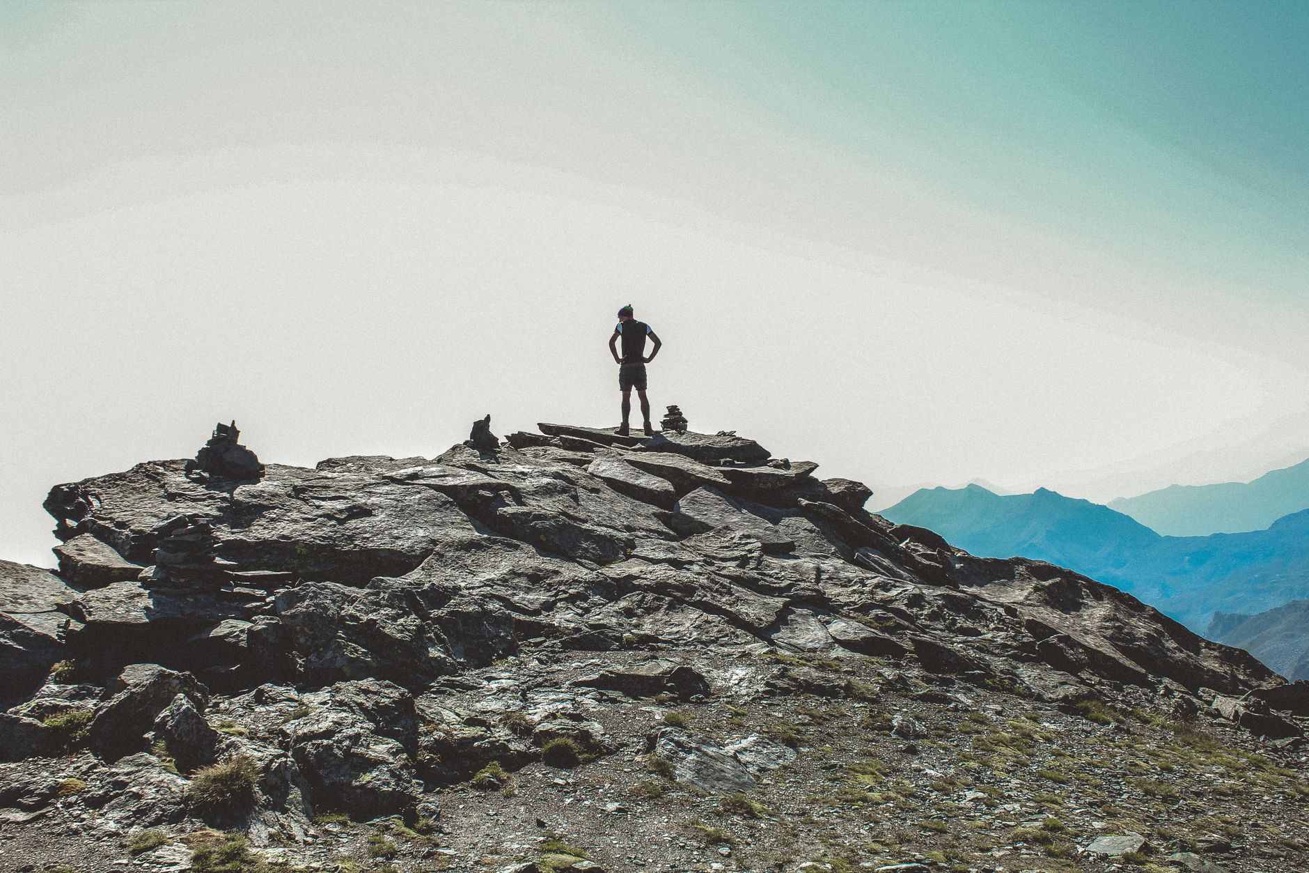 A lone hiker stands atop a rugged mountain peak, gazing at the foggy horizon.