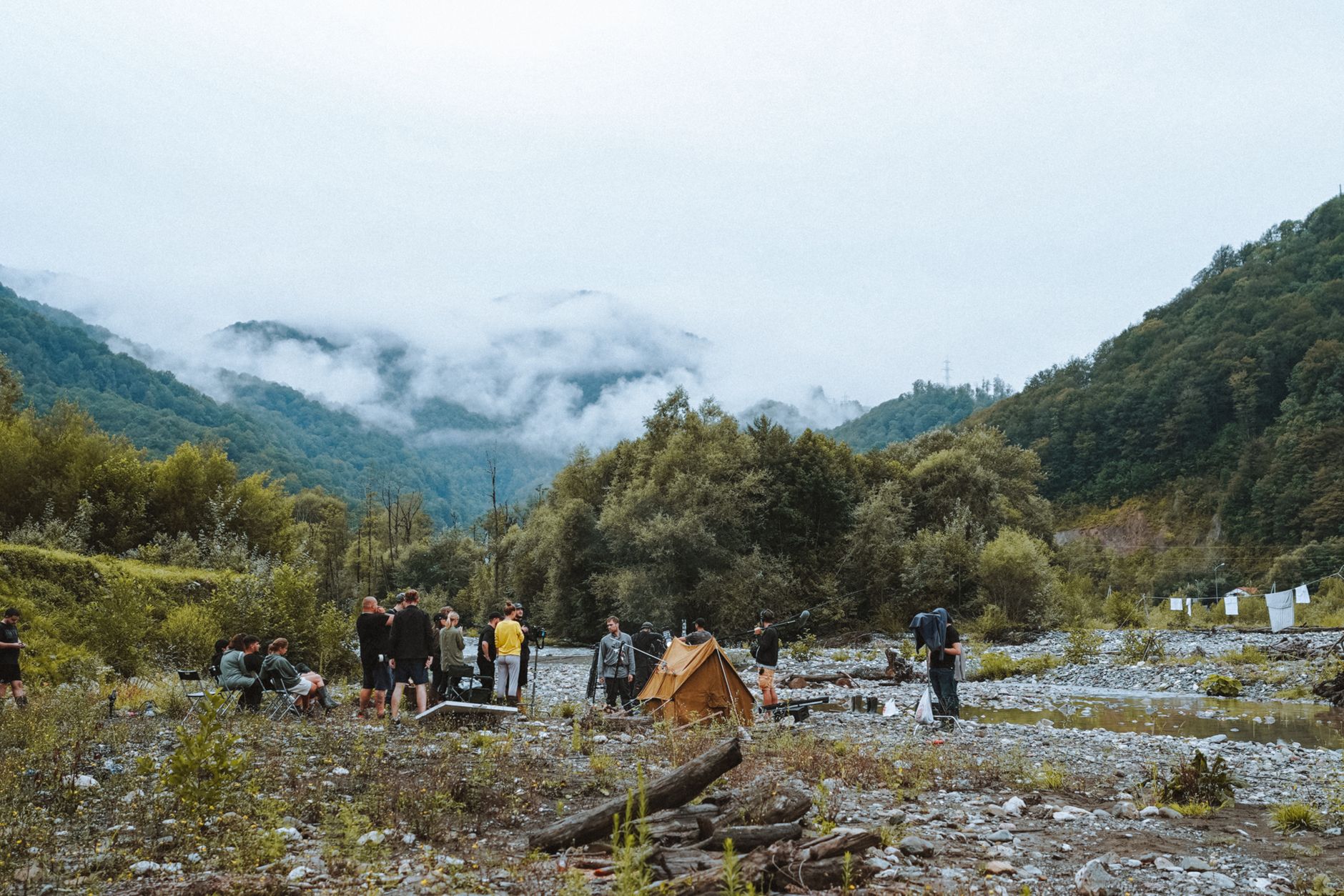 Film crew in a mountain landscape with a tent and misty scenery.