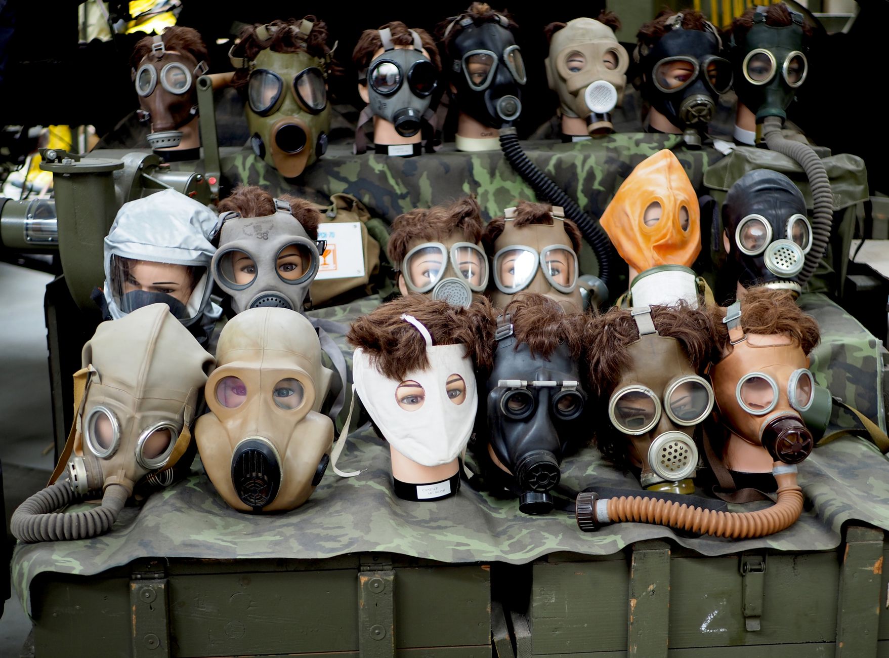 A diverse array of vintage gas masks displayed on mannequins with varied designs and colors.